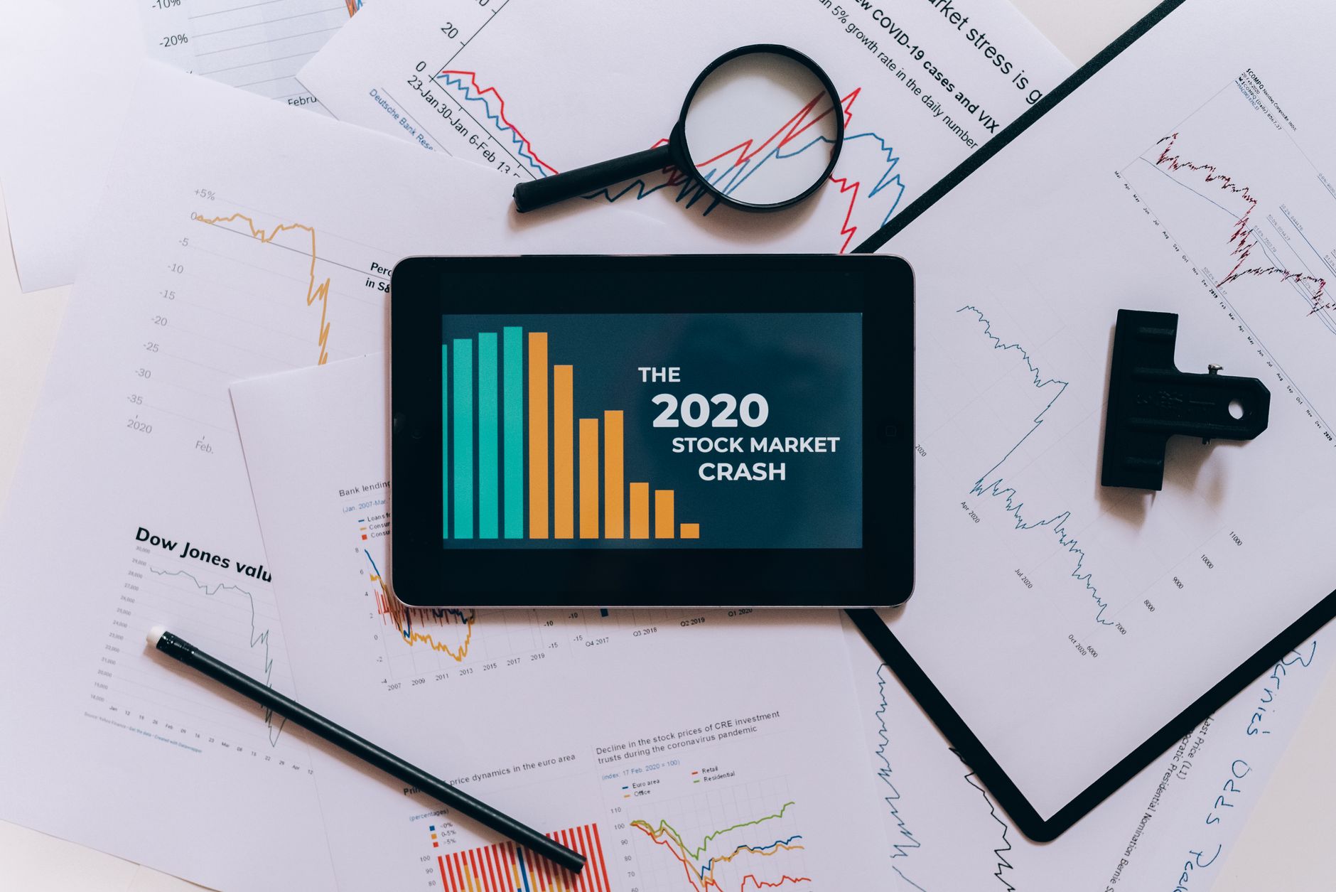 Flat lay of tablet showing 2020 stock market crash with charts and papers.