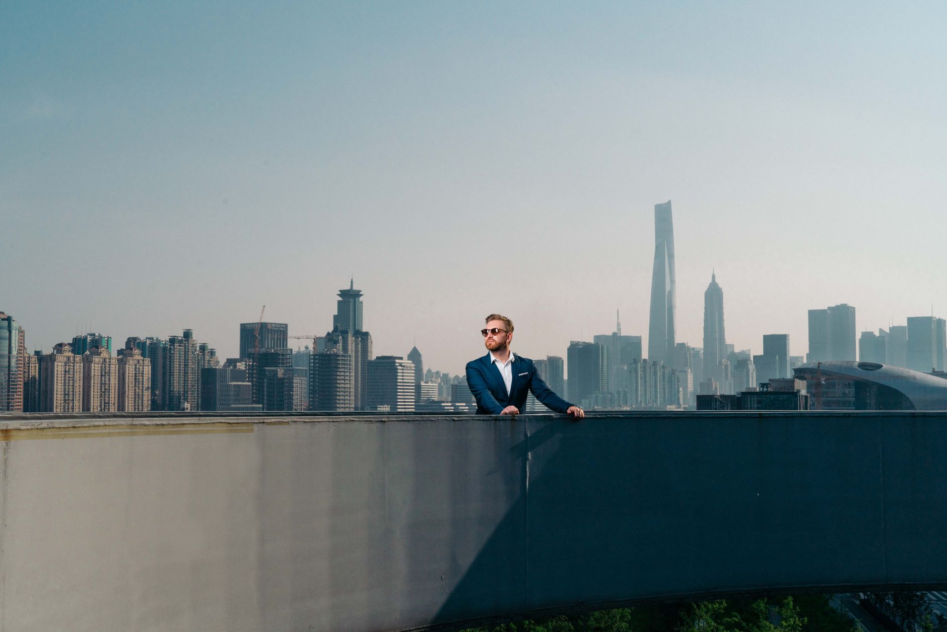 Stylish man in a suit enjoys a rooftop view of the iconic Shanghai skyline on a clear day.