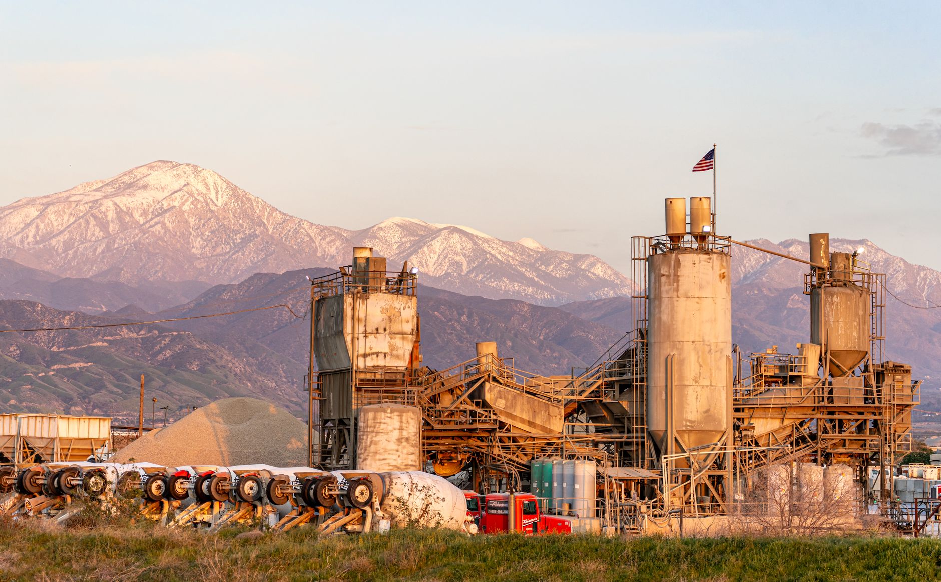 Cement factory in Redlands, CA with mountains and American flag at sunset.