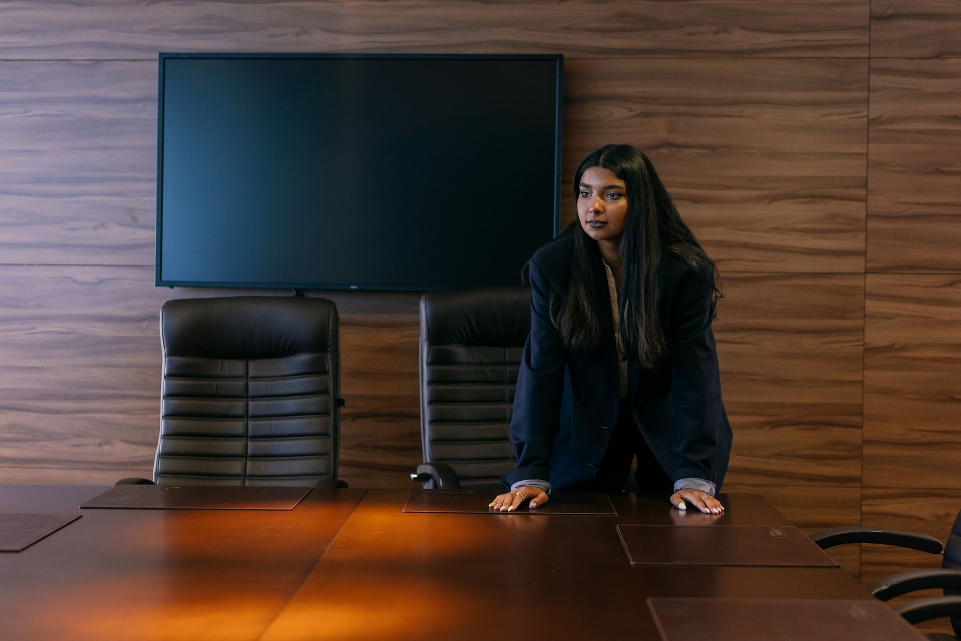Professional woman in corporate attire standing in a sophisticated boardroom setting.