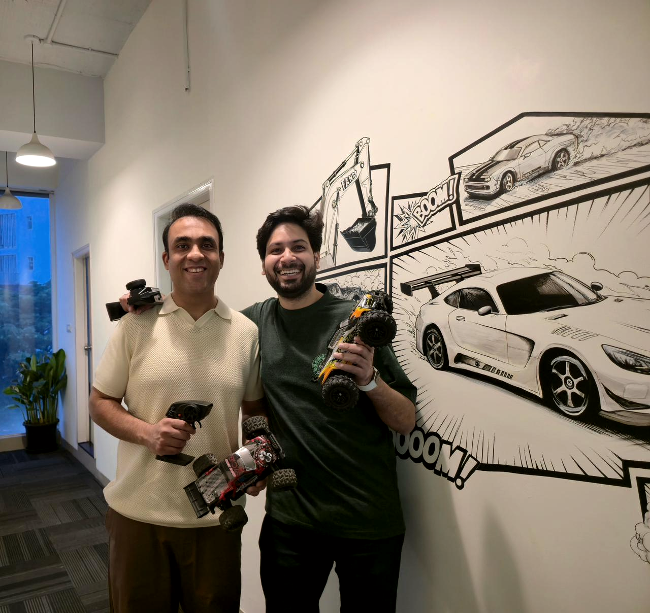 Legend of Toys co-founders Afshaan Siddiqui (left) and Vinay Jaisingh holding RC drift cars, in front of a comic-book mural of cars.