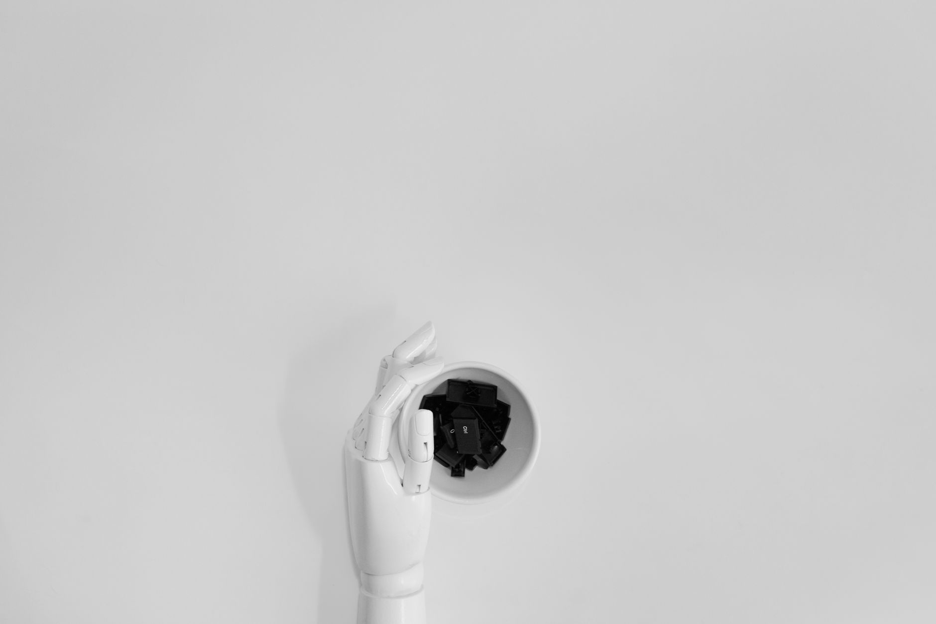 A robotic hand grasping black keyboard keys in a minimalist setting.