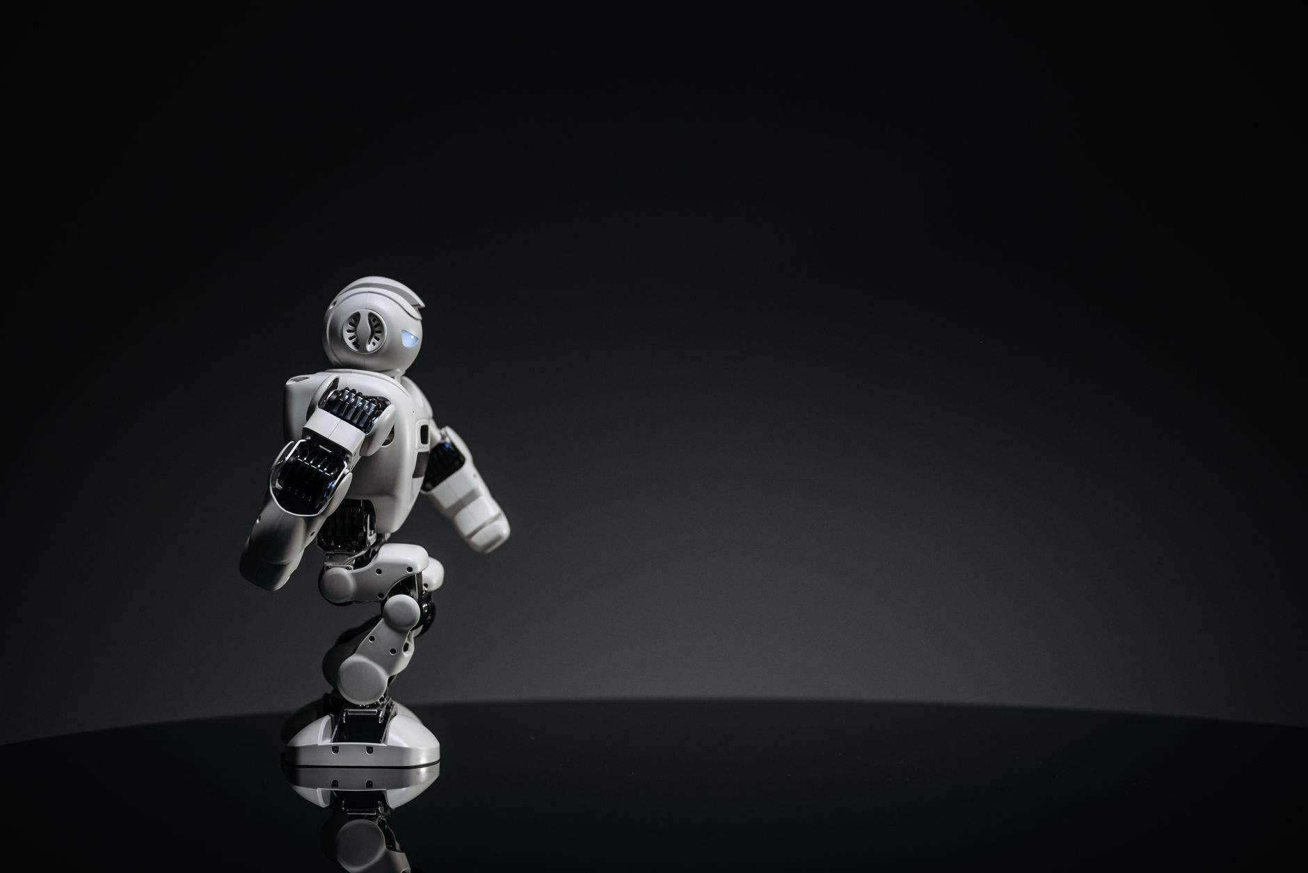 A sleek white toy robot poised elegantly against a dark studio backdrop.