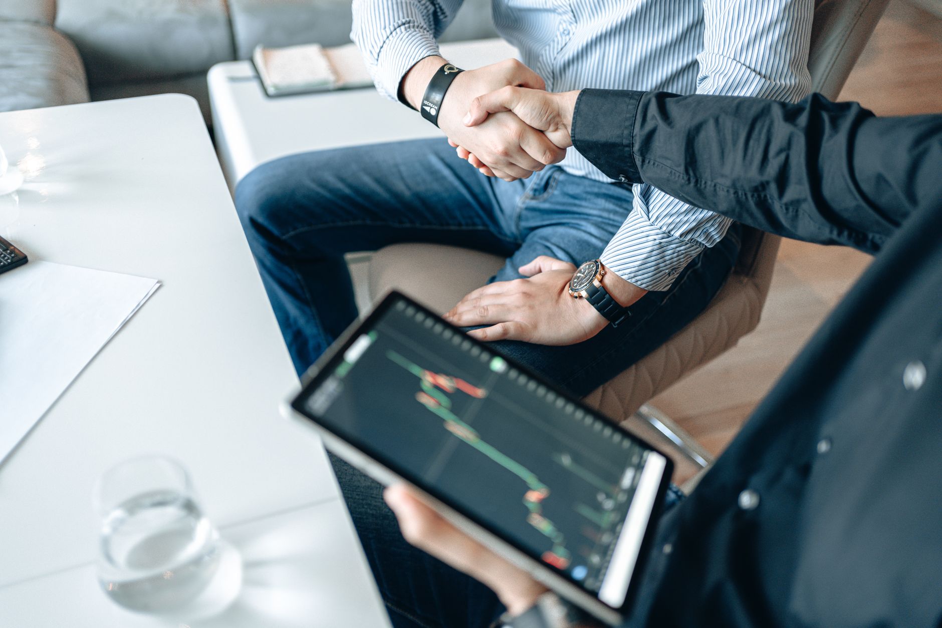 Business professionals shaking hands with a tablet displaying financial graphs.