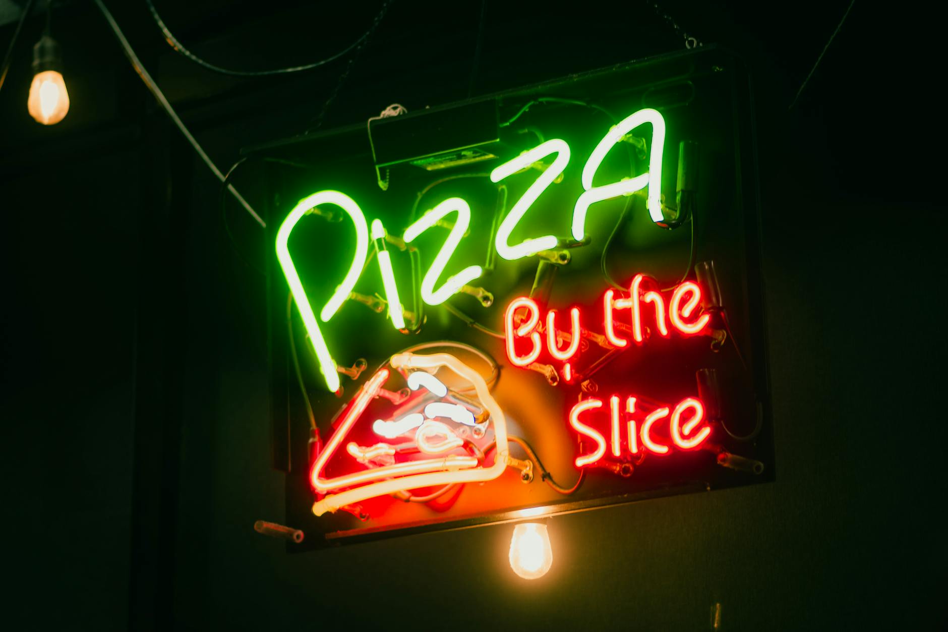 Vibrant neon sign advertising pizza by the slice with iconic colors.
