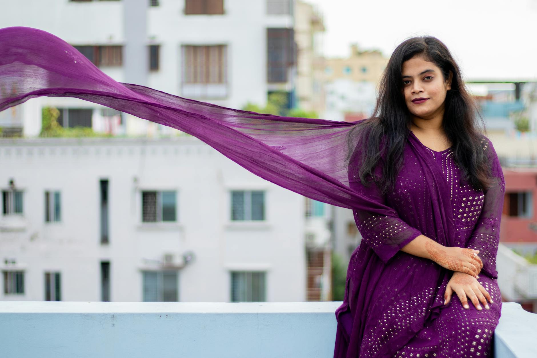 Portrait of a woman in a purple traditional sari sitting outdoors, showcasing elegance.