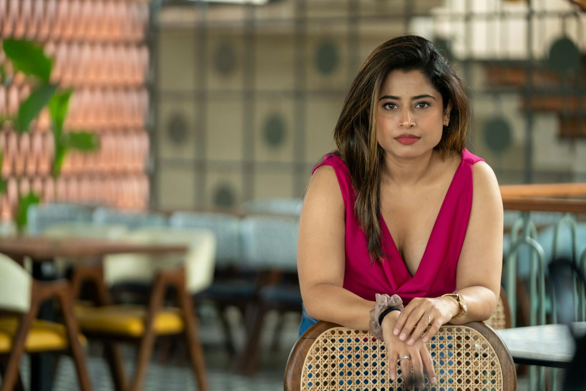 Woman in pink top seated in a stylish cafe, showcasing modern lifestyle and fashion.