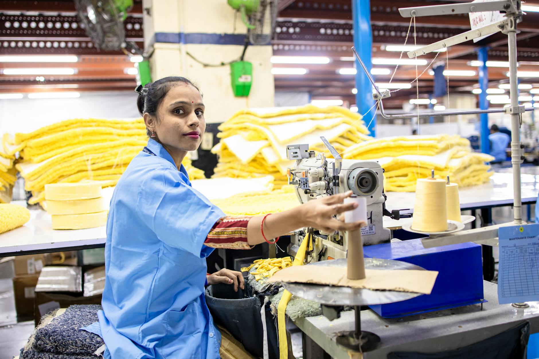 Woman working in a textile factory at sewing machine, surrounded by yellow fabrics.