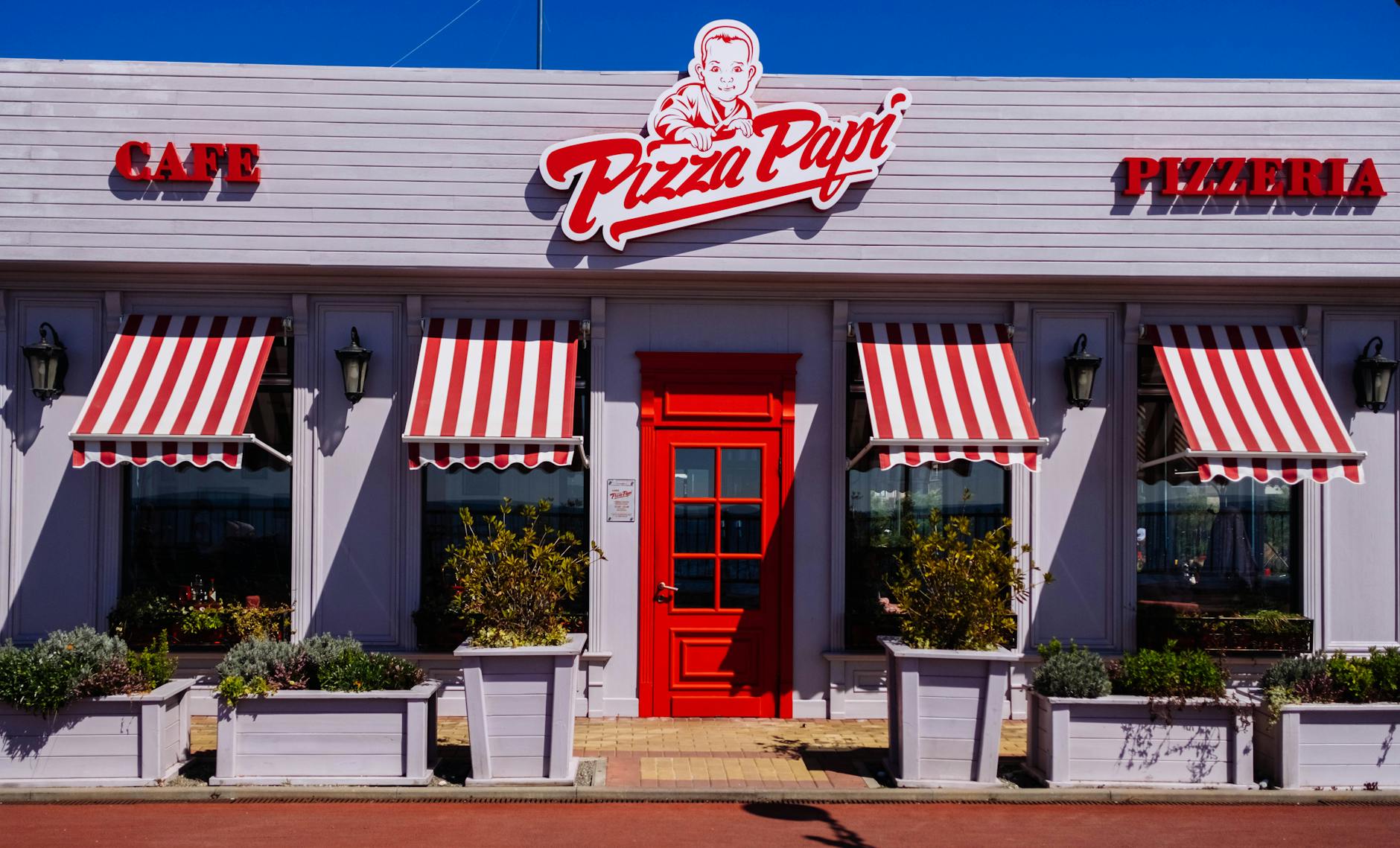 A vibrant facade of Pizza Papi pizzeria with red and white striped awnings in Sochi.