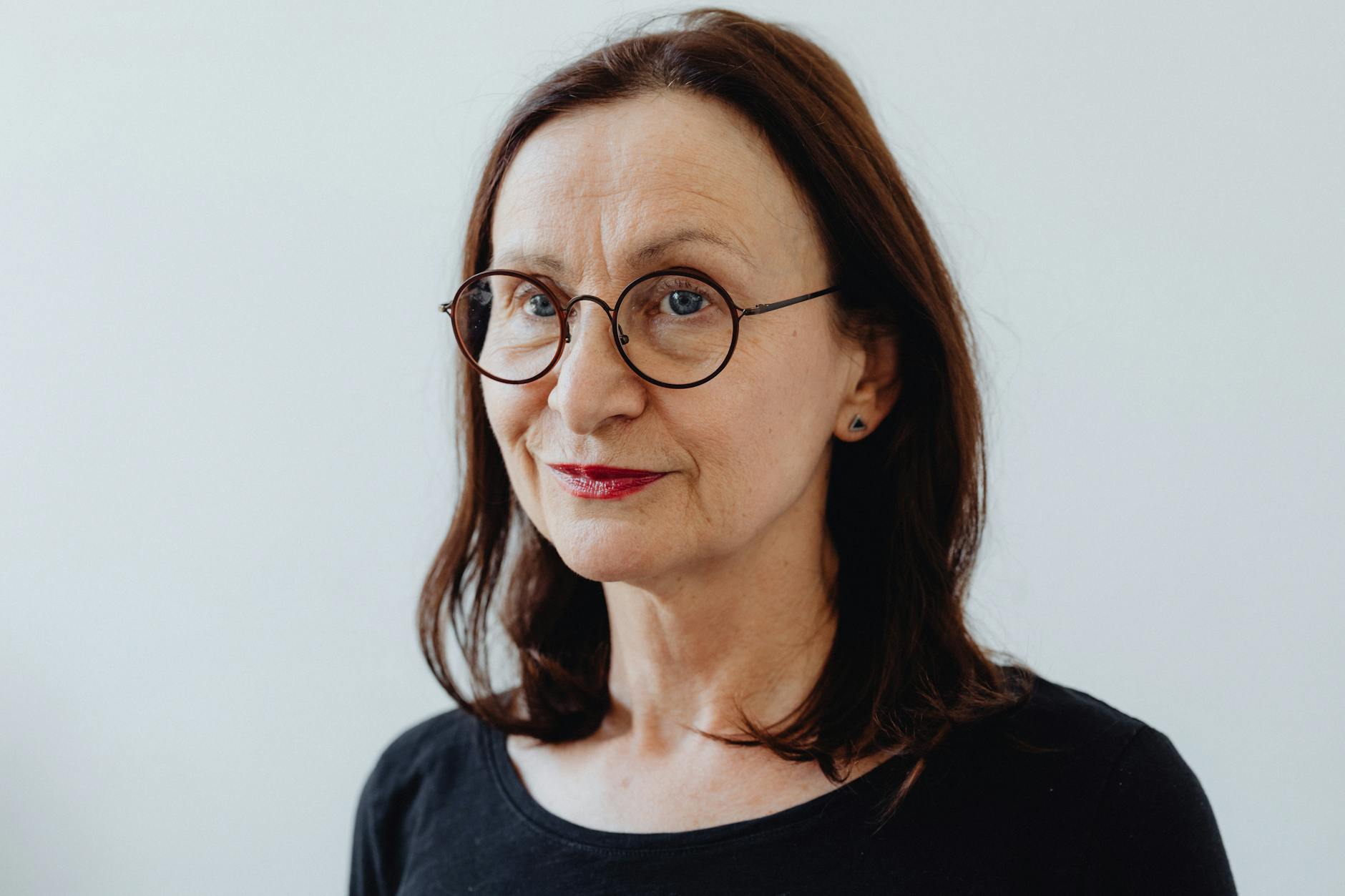Headshot of a smiling elderly woman with eyeglasses and a black shirt against a white background.