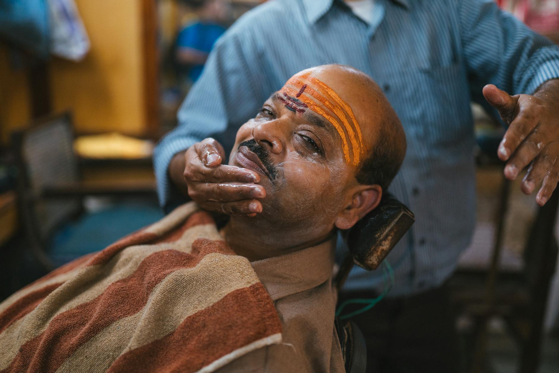 A man receiving a traditional shave in a barber shop in Varanasi, showcasing local customs.
