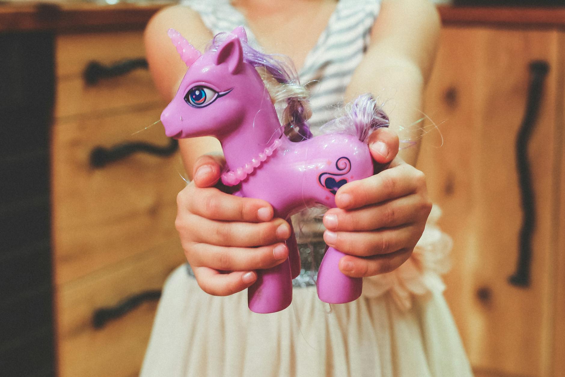 Close-up of a child holding a pink toy unicorn indoors, showcasing playful innocence.