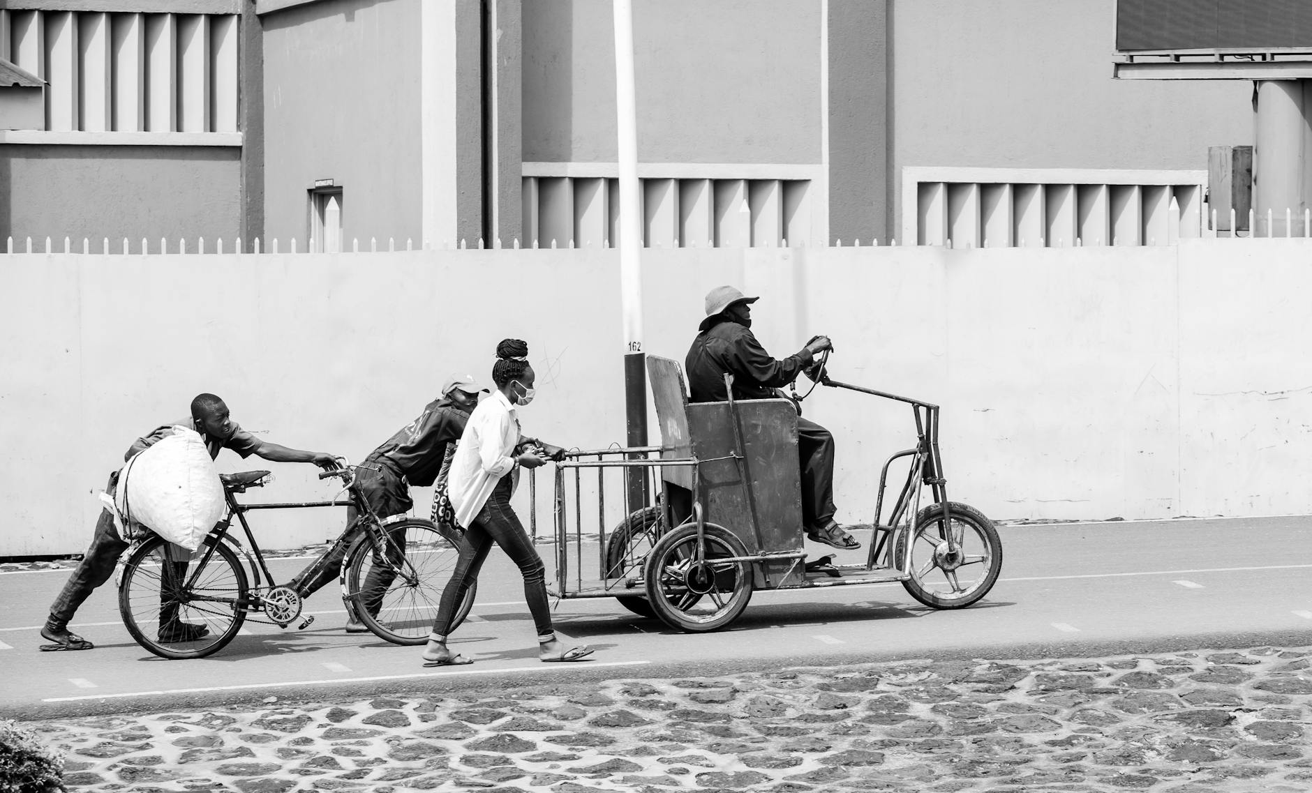 Black and white photo of people moving tricycles and bicycles in an urban setting.