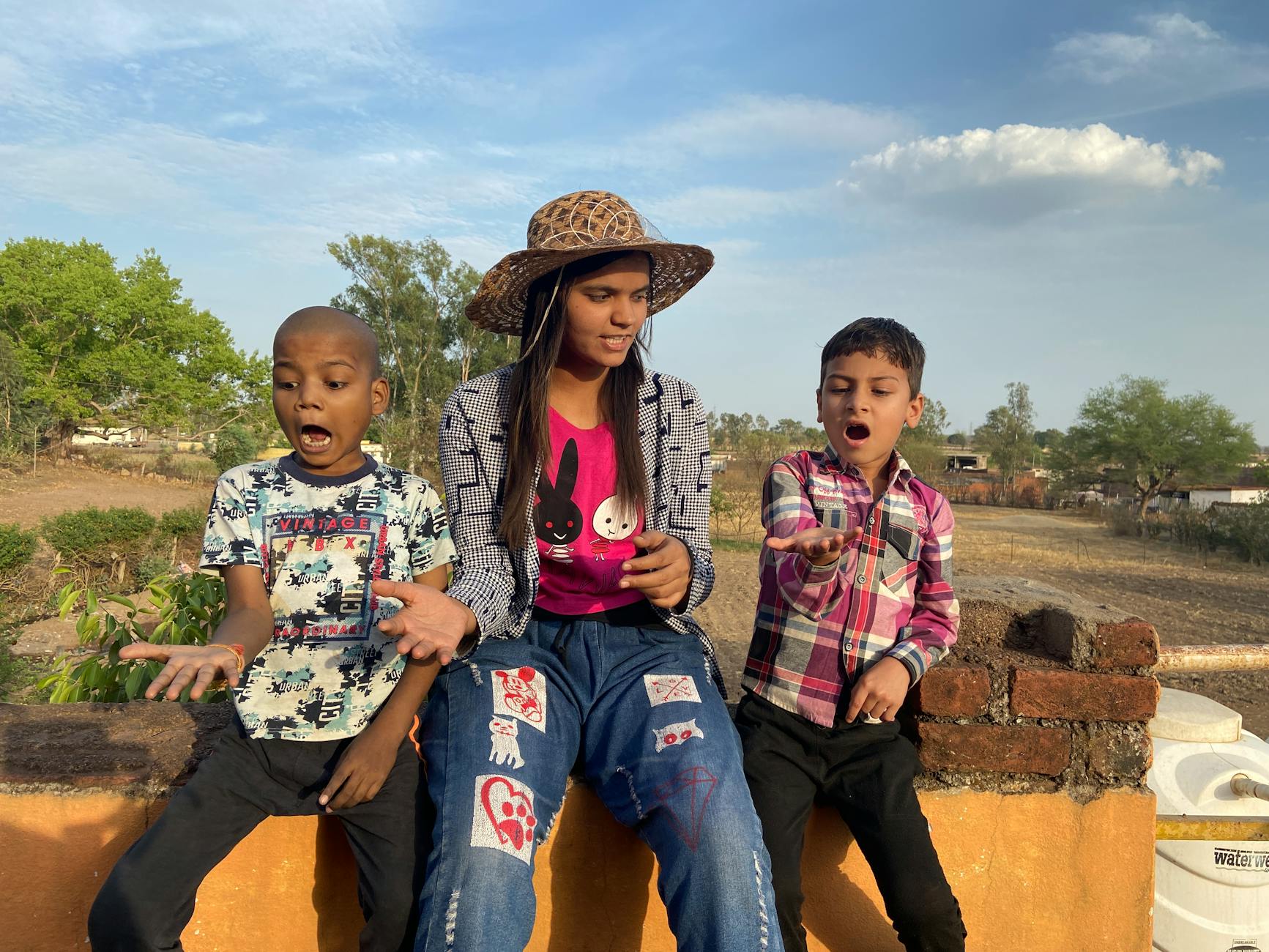 Three children expressing surprise while playing outdoors in Umri, India.