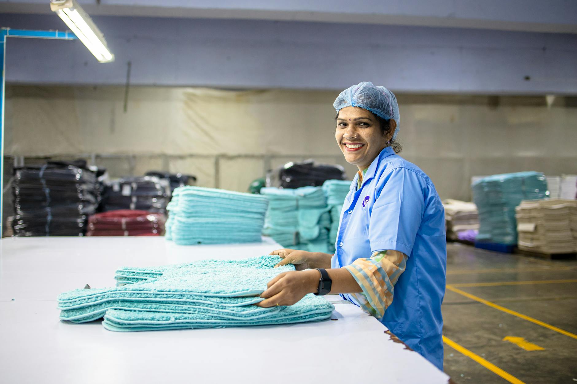 A happy textile worker in a factory is seen folding fabrics, showcasing industrious work environment.