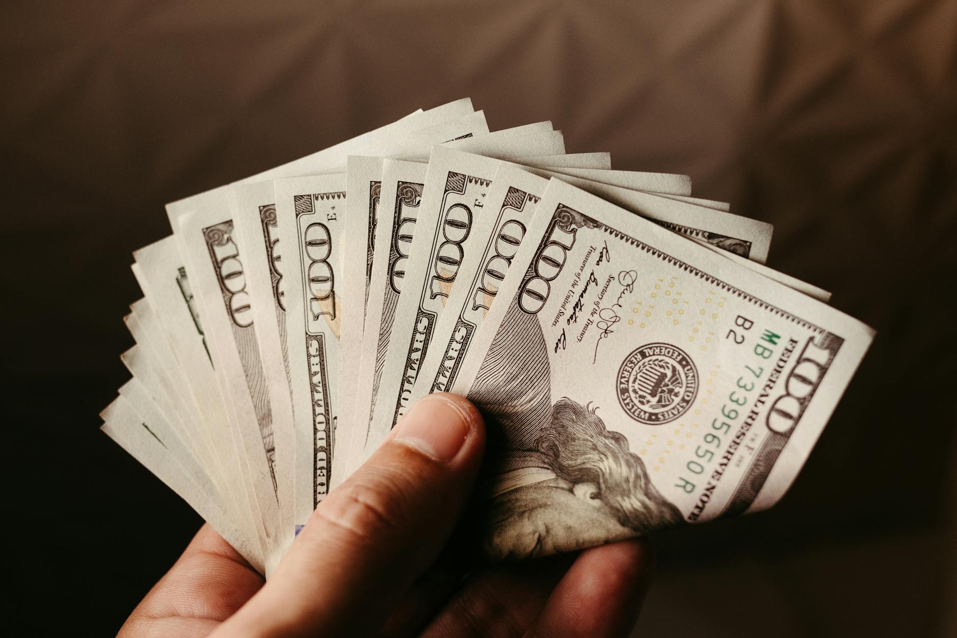 Fan of US hundred dollar bills held in hand, symbolizing wealth and finance.