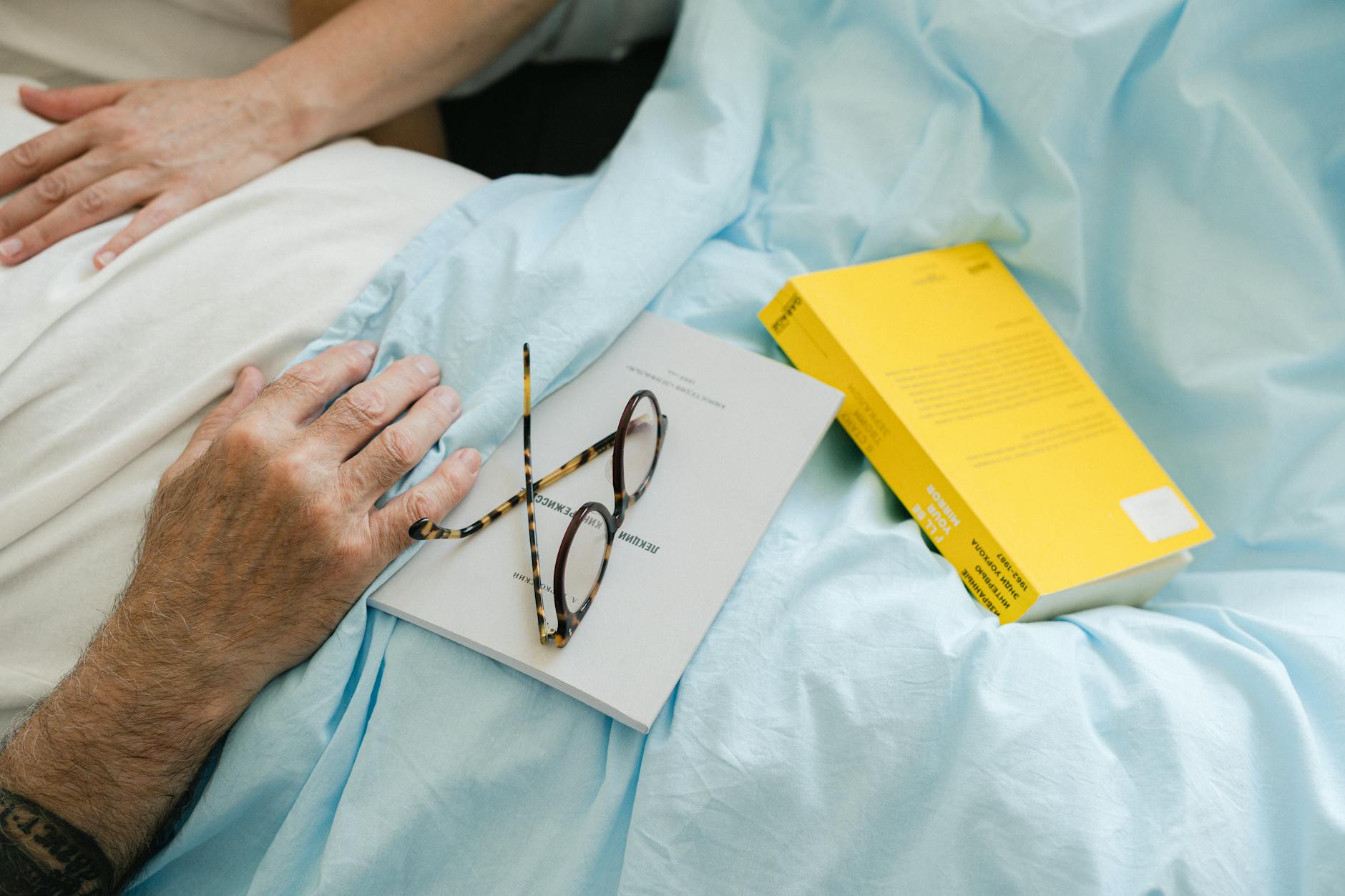 Books and eyeglasses on a cozy bed setup, perfect for a relaxing reading moment.