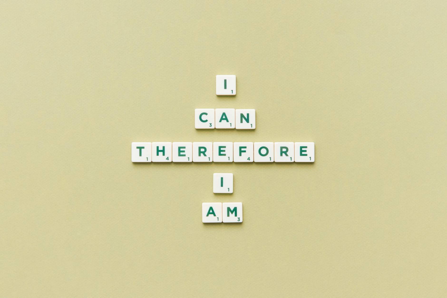 Inspirational phrase 'I Can Therefore I Am' arranged using Scrabble tiles on a green background.