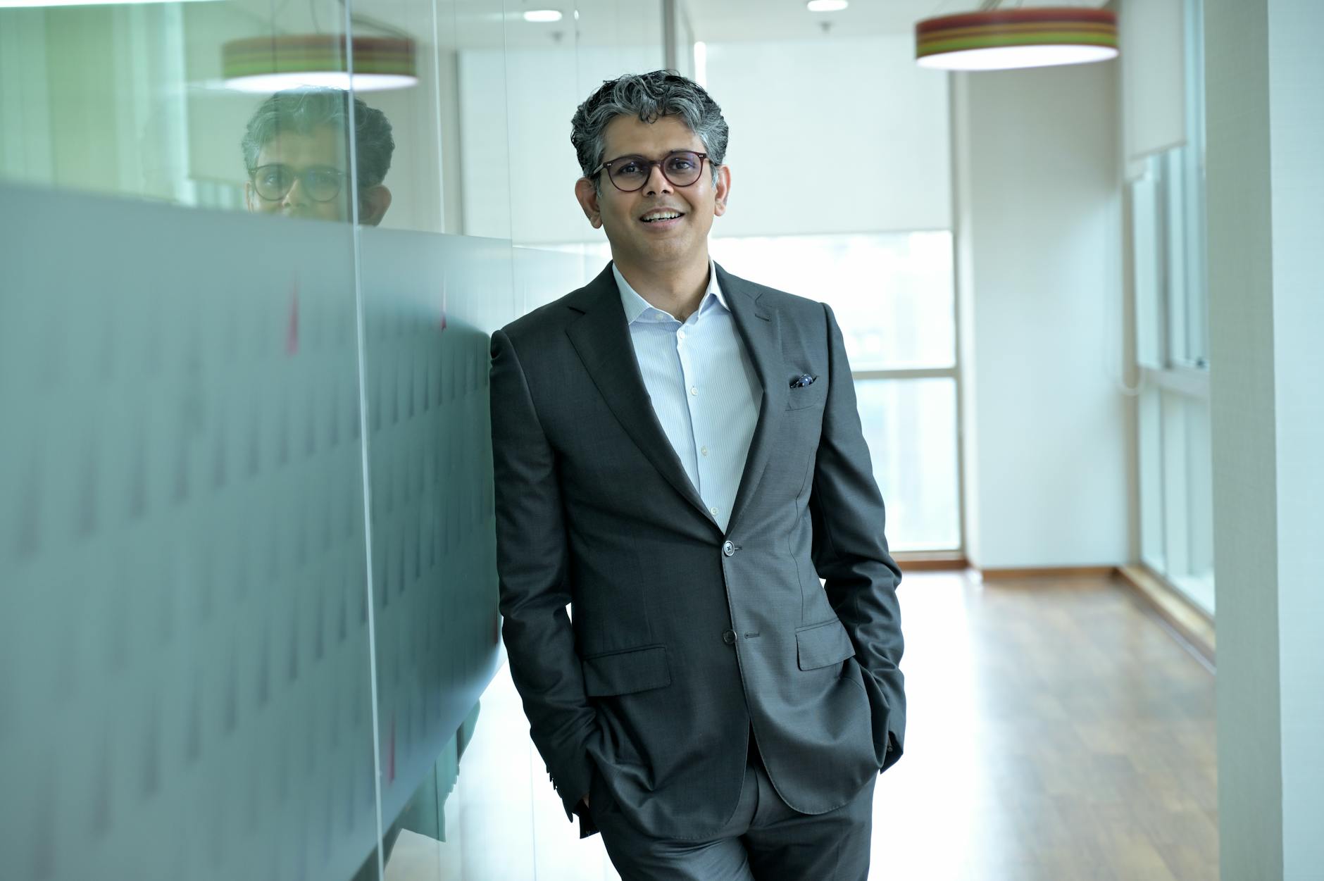 Smiling businessman standing confidently in a modern office hallway, wearing a suit.
