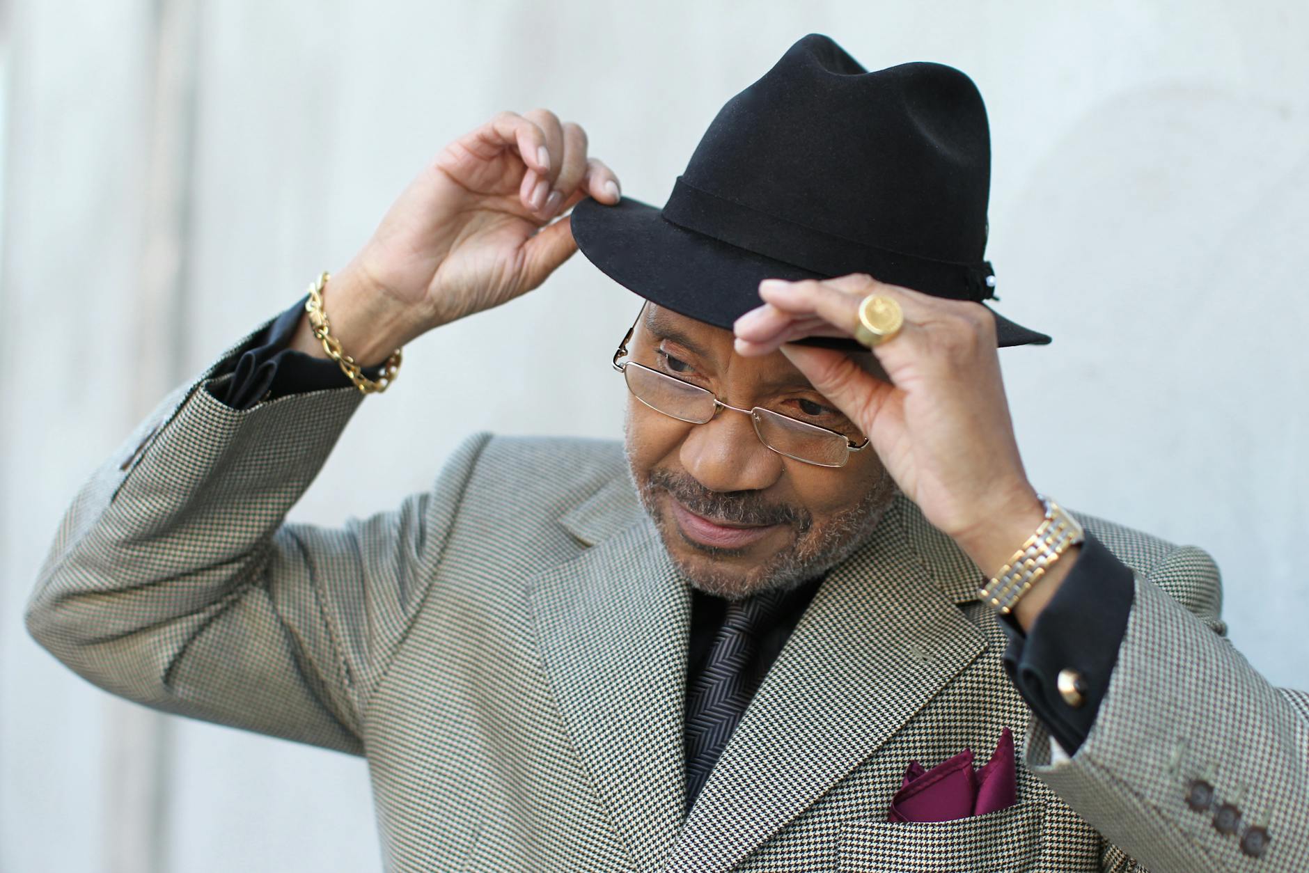 Portrait of a fashionable man wearing a suit and fedora, adjusting his hat with a confident expression.