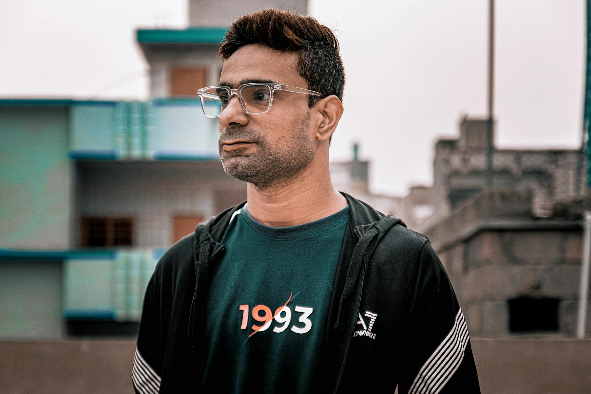 Portrait of an adult man wearing eyeglasses and a casual outfit in an urban outdoor setting.