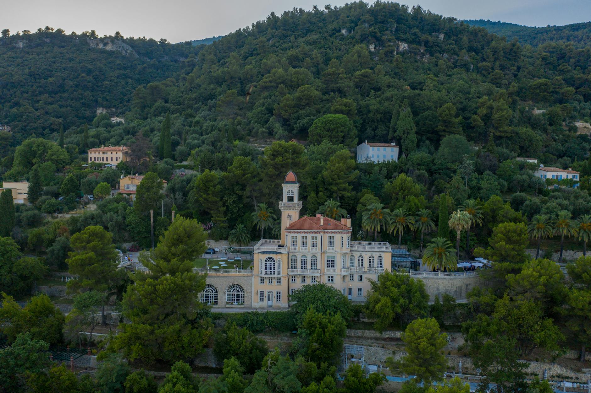 Charming aerial view of a historic mansion nestled within lush, green hills surrounded by vibrant trees.