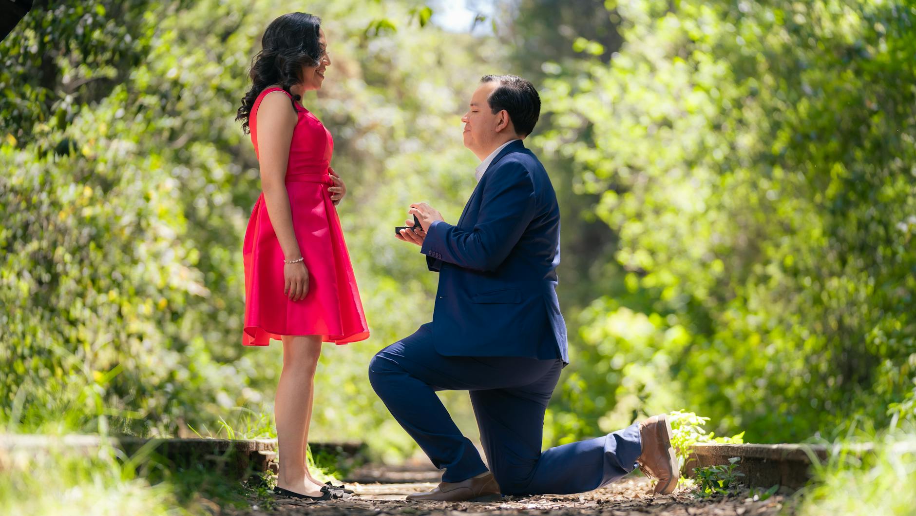 Man proposes on one knee to woman in a romantic forest setting.