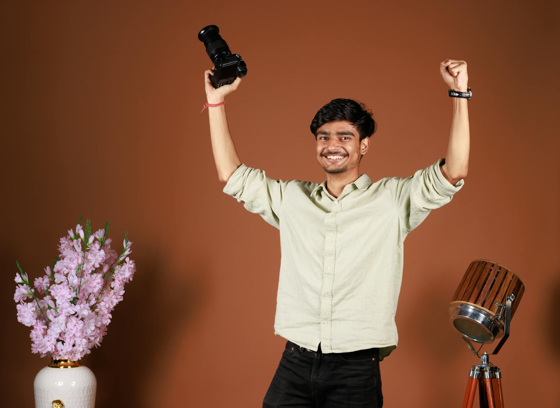 A joyful young photographer triumphantly raises a camera in a studio setting.