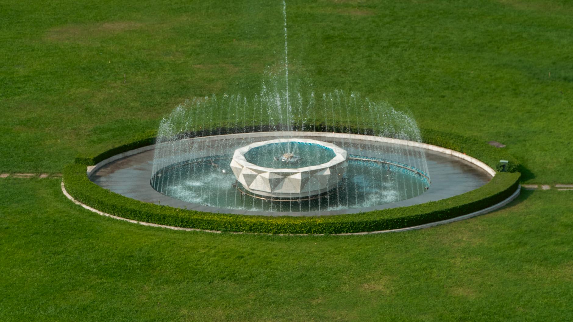 Aerial photo of an elegant geometric fountain surrounded by green grass.
