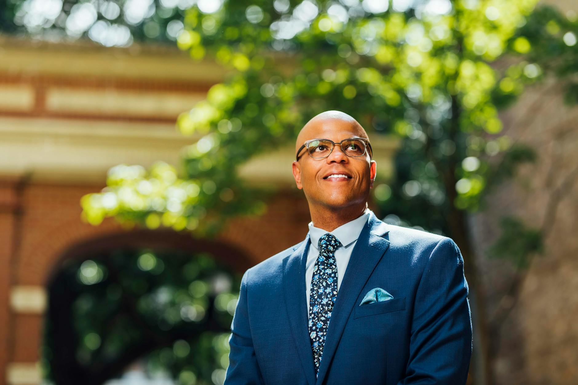 Professional man smiling in a blue suit outdoors with bokeh effect, embodying confidence and success.