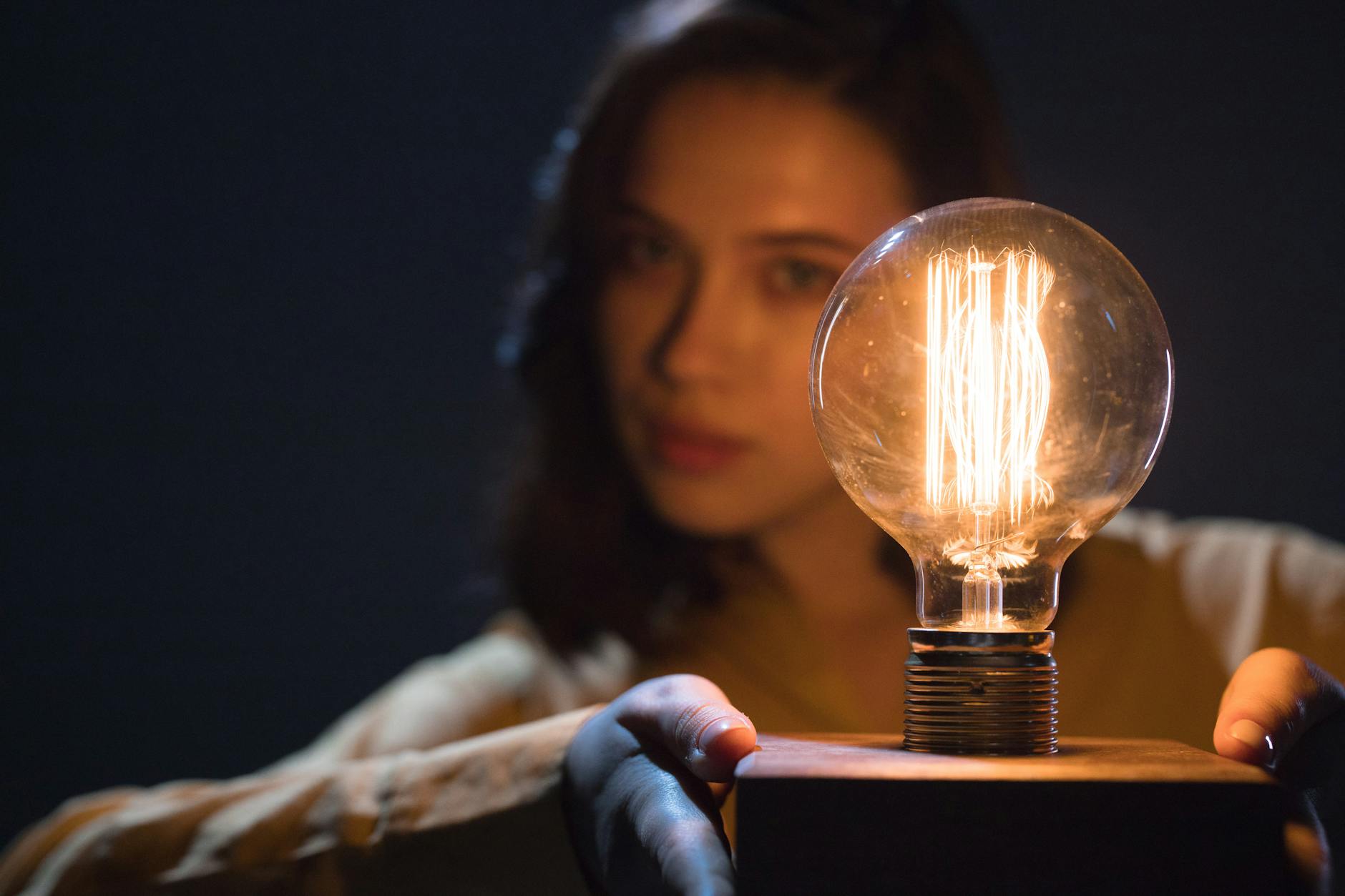 Close-up of a glowing light bulb held by a woman creating an artistic and moody atmosphere.