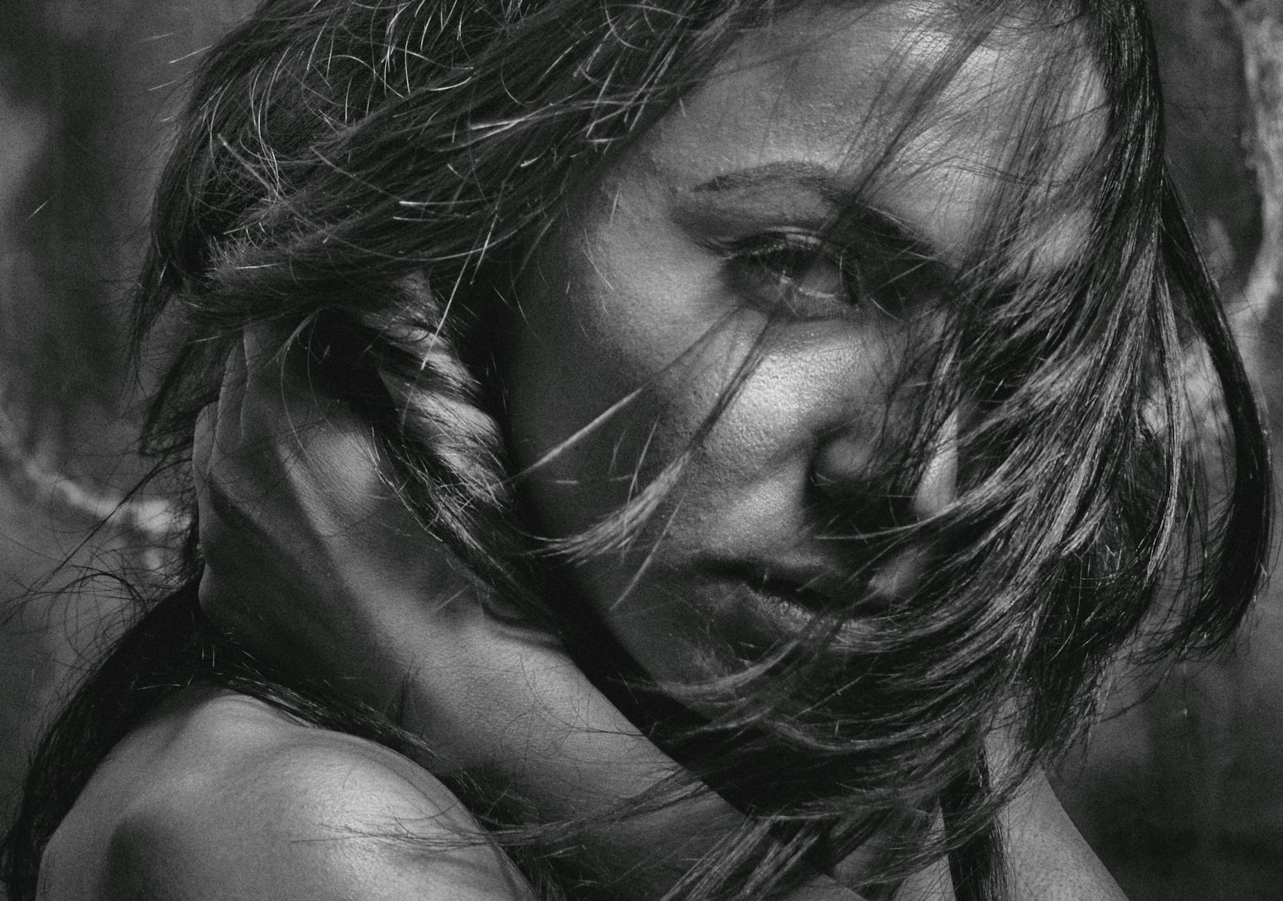 Intense black and white portrait of a woman with hair in motion, captured with dramatic lighting.
