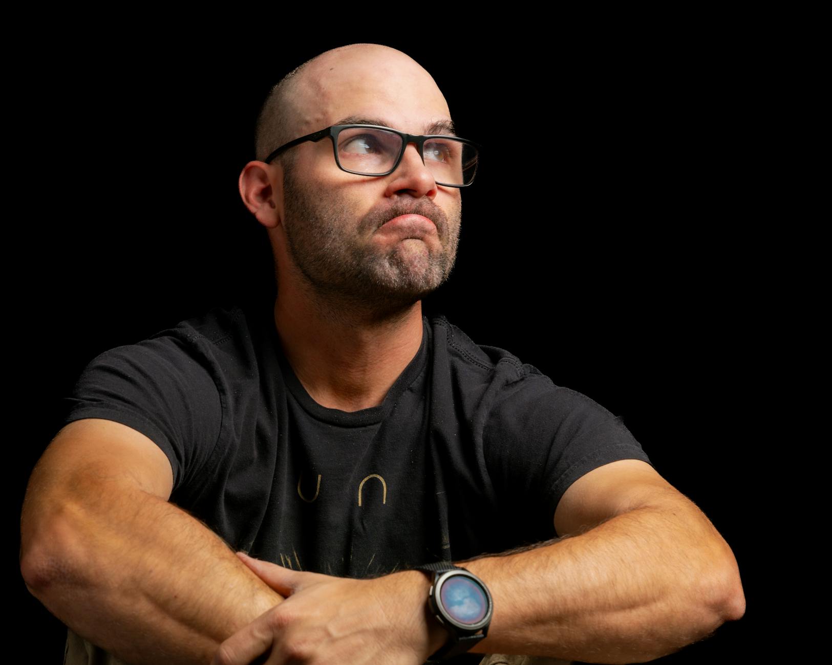 Thoughtful man with glasses in a dark setting, displaying a contemplative expression. Ideal for lifestyle imagery.