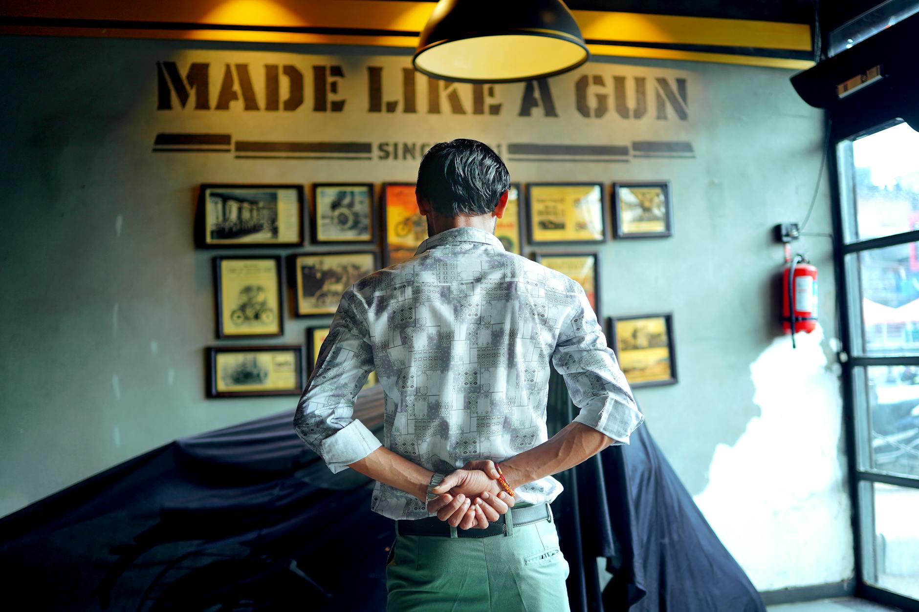 A man stands indoors examining framed motorcycle photos on a wall, creating a contemplative mood.