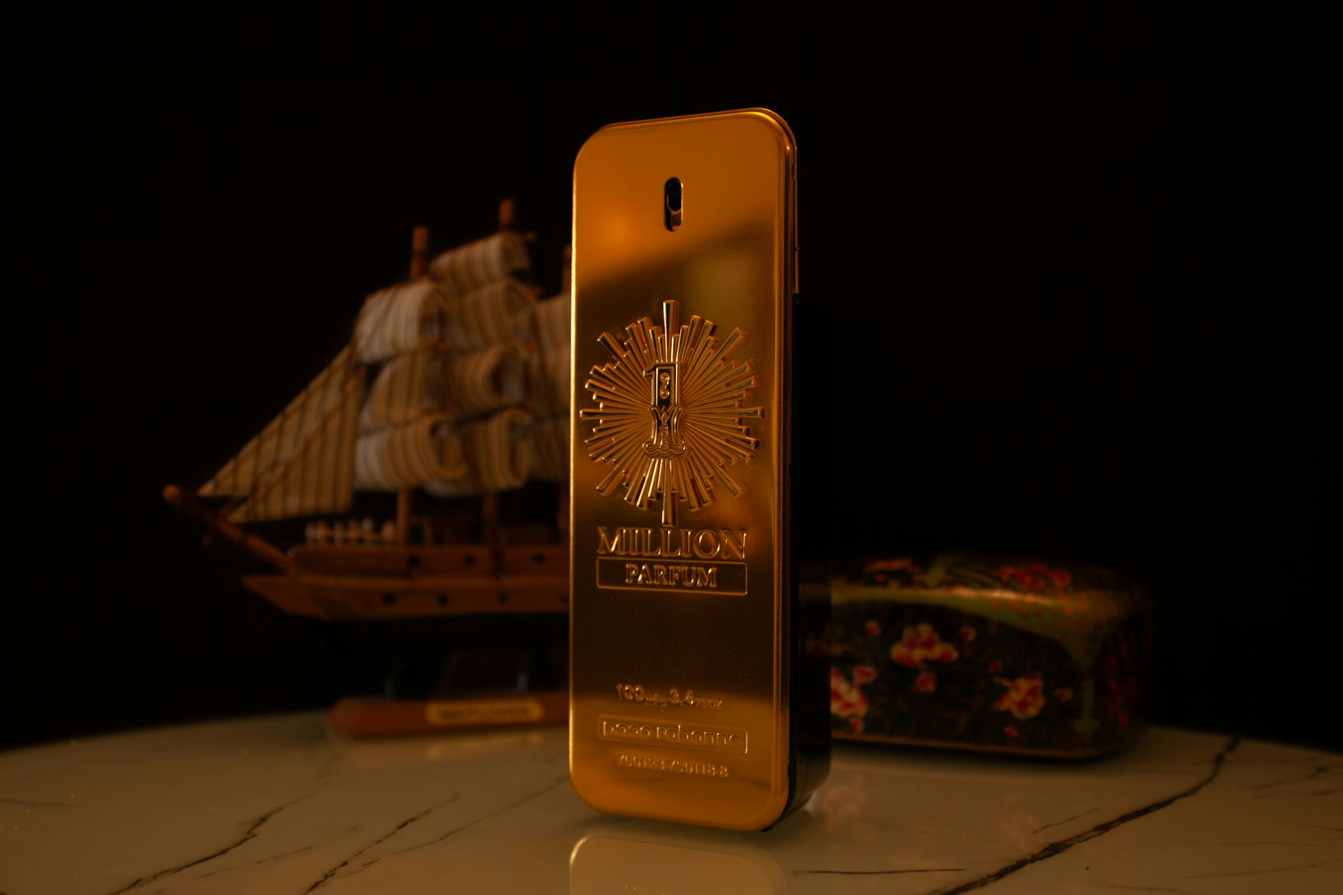 Elegant golden perfume bottle with a ship and floral box in the background.