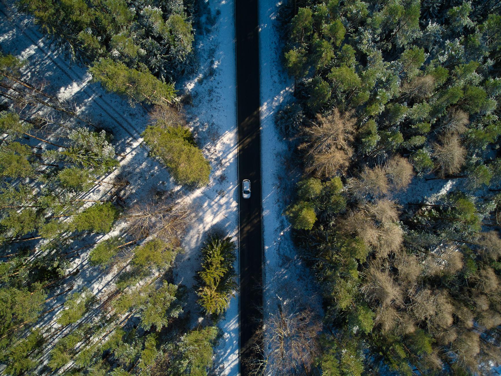 Drone shot of a snowy forest road in Ilmenau, Germany, surrounded by coniferous trees.