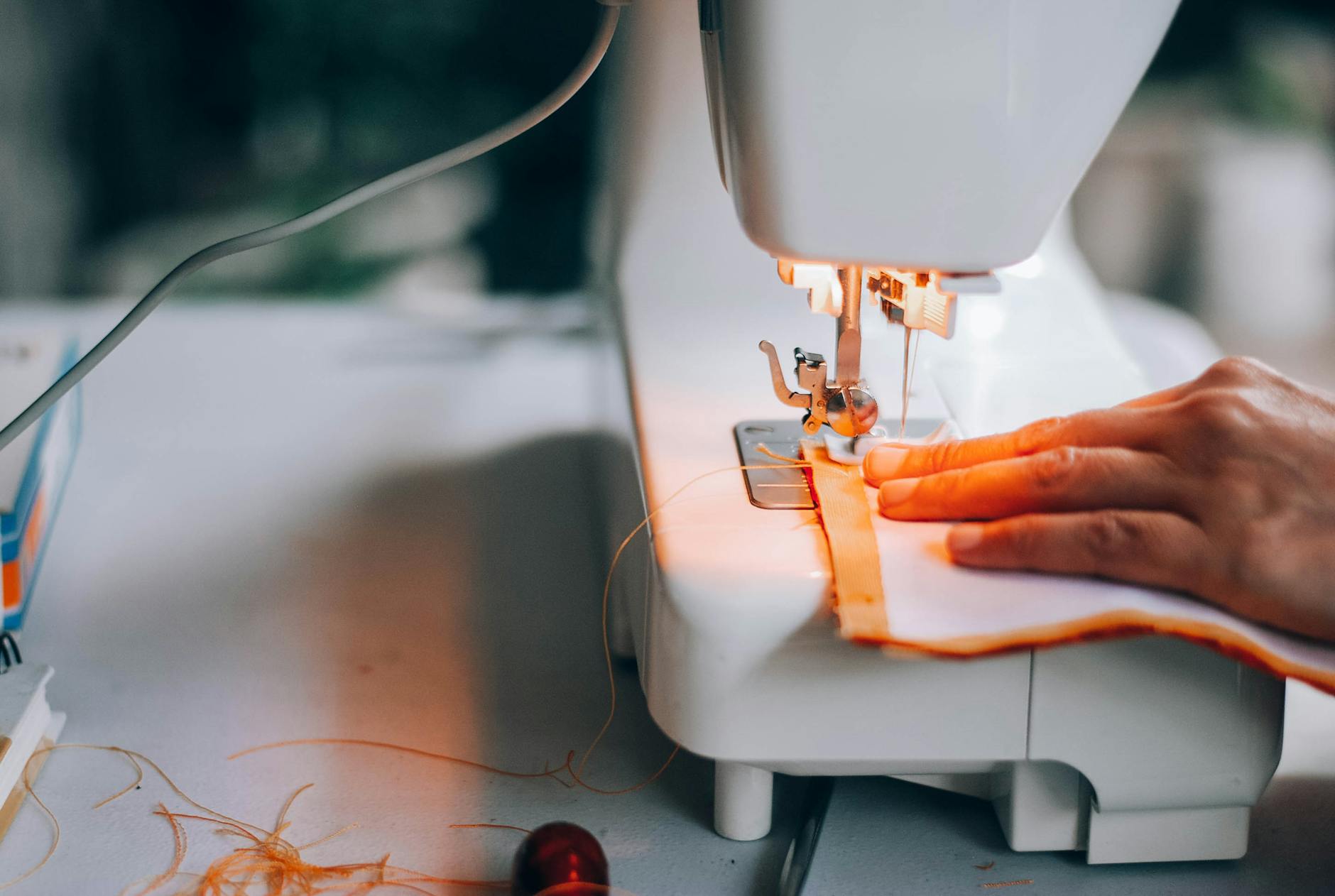 A close-up view of a hand guiding fabric through a sewing machine, highlighting the sewing process.