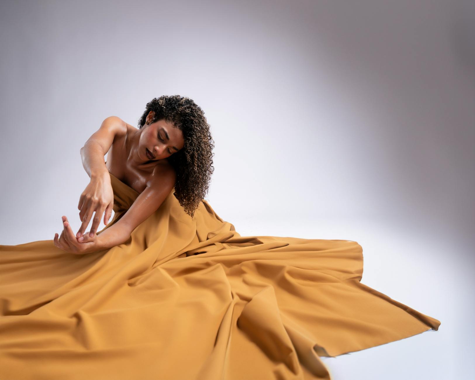 A beautiful woman with curly hair poses elegantly with a yellow dress in a studio setting.