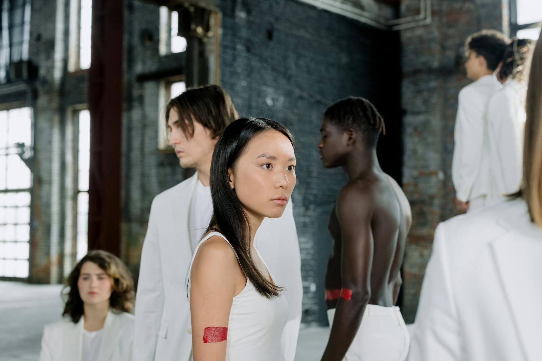 Group of diverse models in white outfits posing in an industrial space, showcasing modern fashion and diversity.