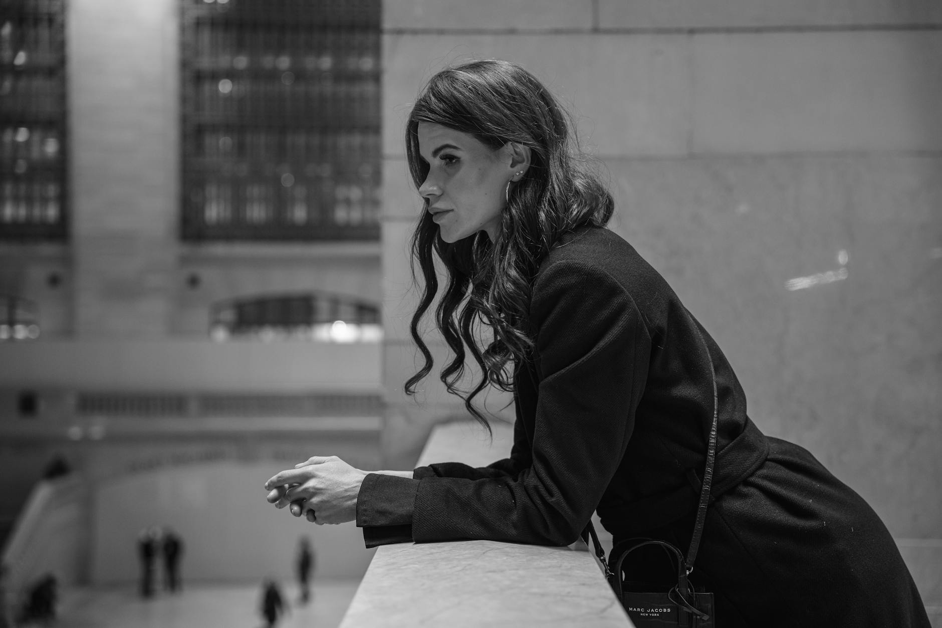 Elegant woman in black coat at Grand Central Terminal, NYC, in a film noir style setting.