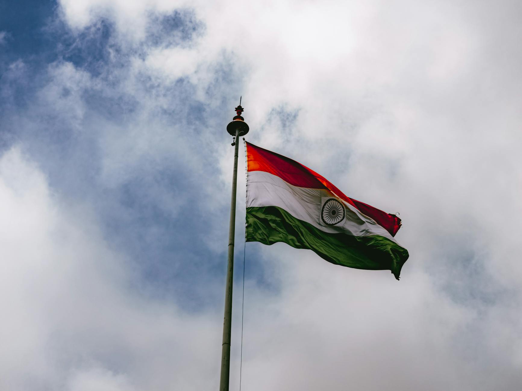 The Indian flag waves proudly against a backdrop of dense, cloudy sky.