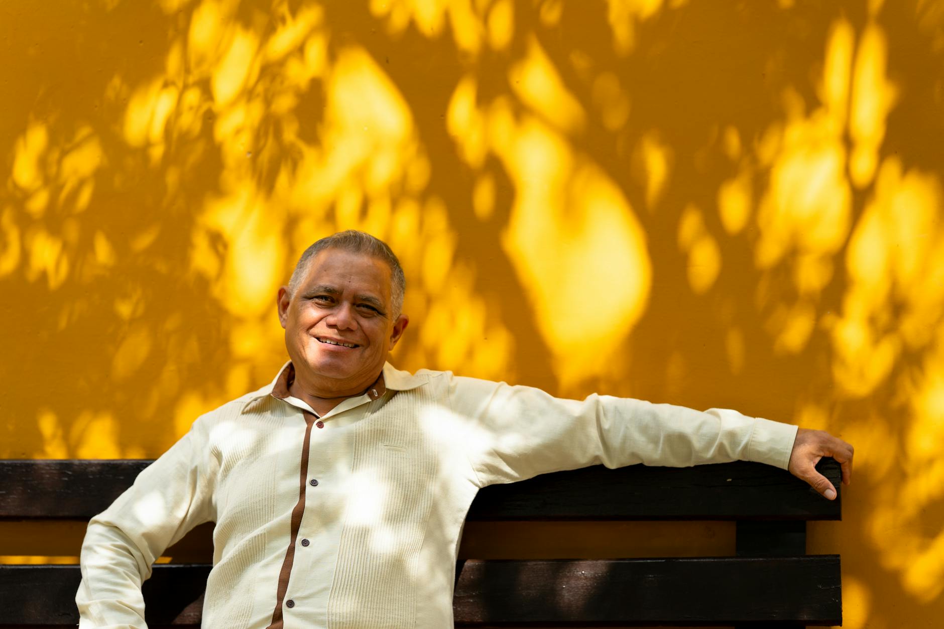 Smiling adult man sitting on a bench against a warm yellow wall in Merida, Yucatan, Mexico.