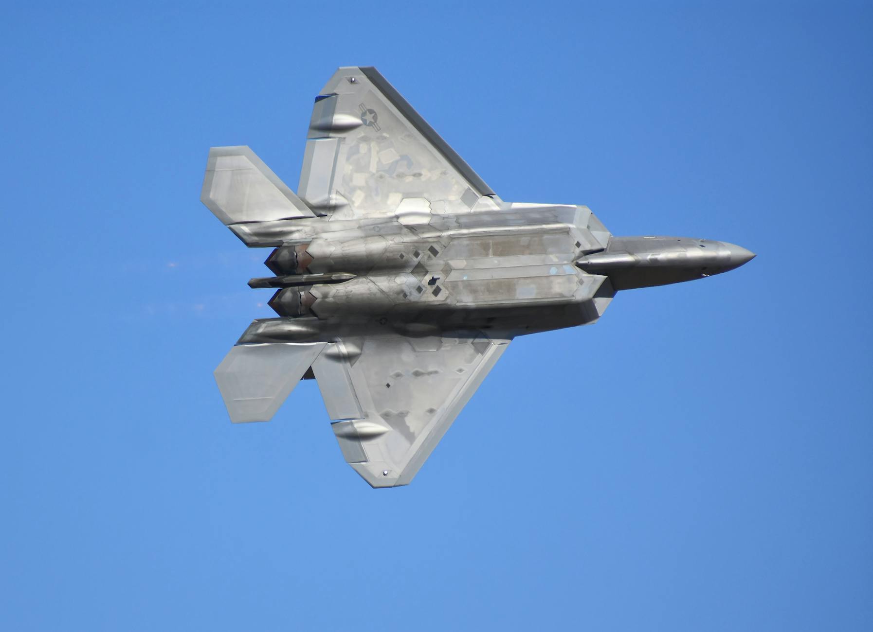 A striking shot of an F-22 Raptor jet fighter in flight against a clear blue sky.