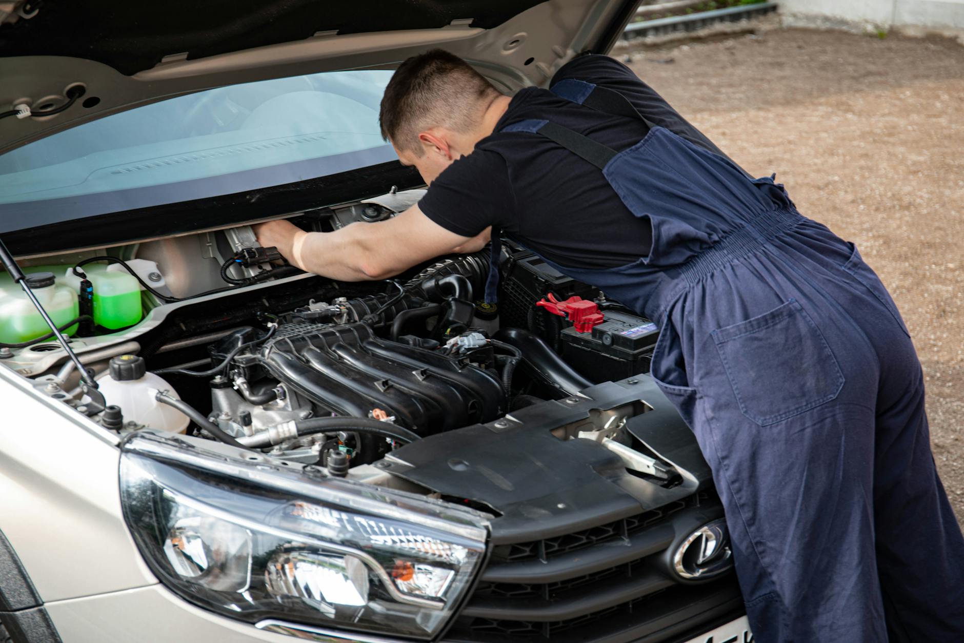 A mechanic focuses on car engine repair in outdoor setting, showcasing precision.