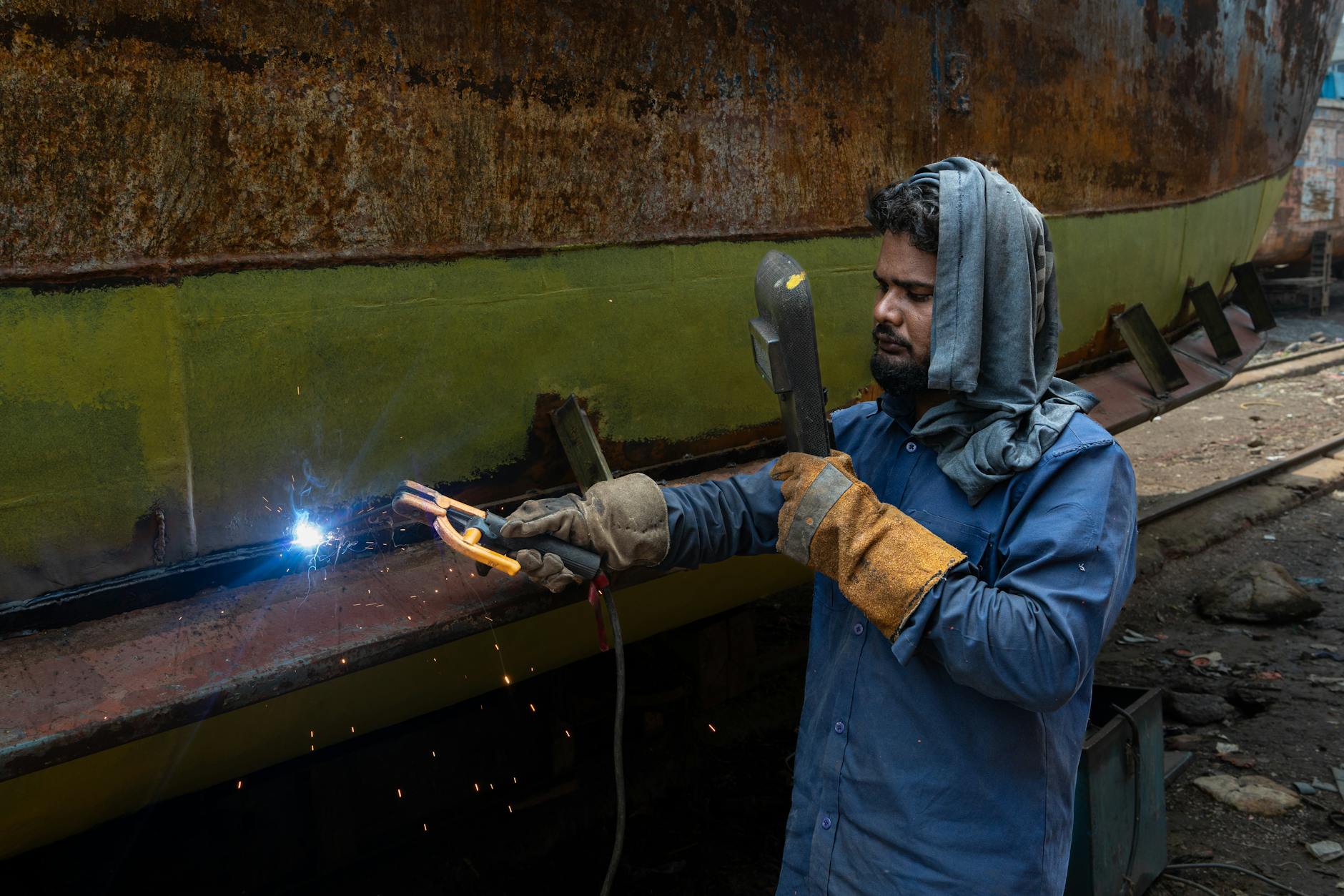 A skilled worker engaged in welding on a ship underbelly, showcasing industrial craftsmanship.