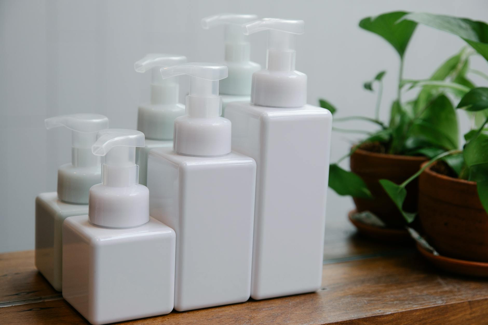 Elegant arrangement of white pump bottles on wooden table near houseplants.