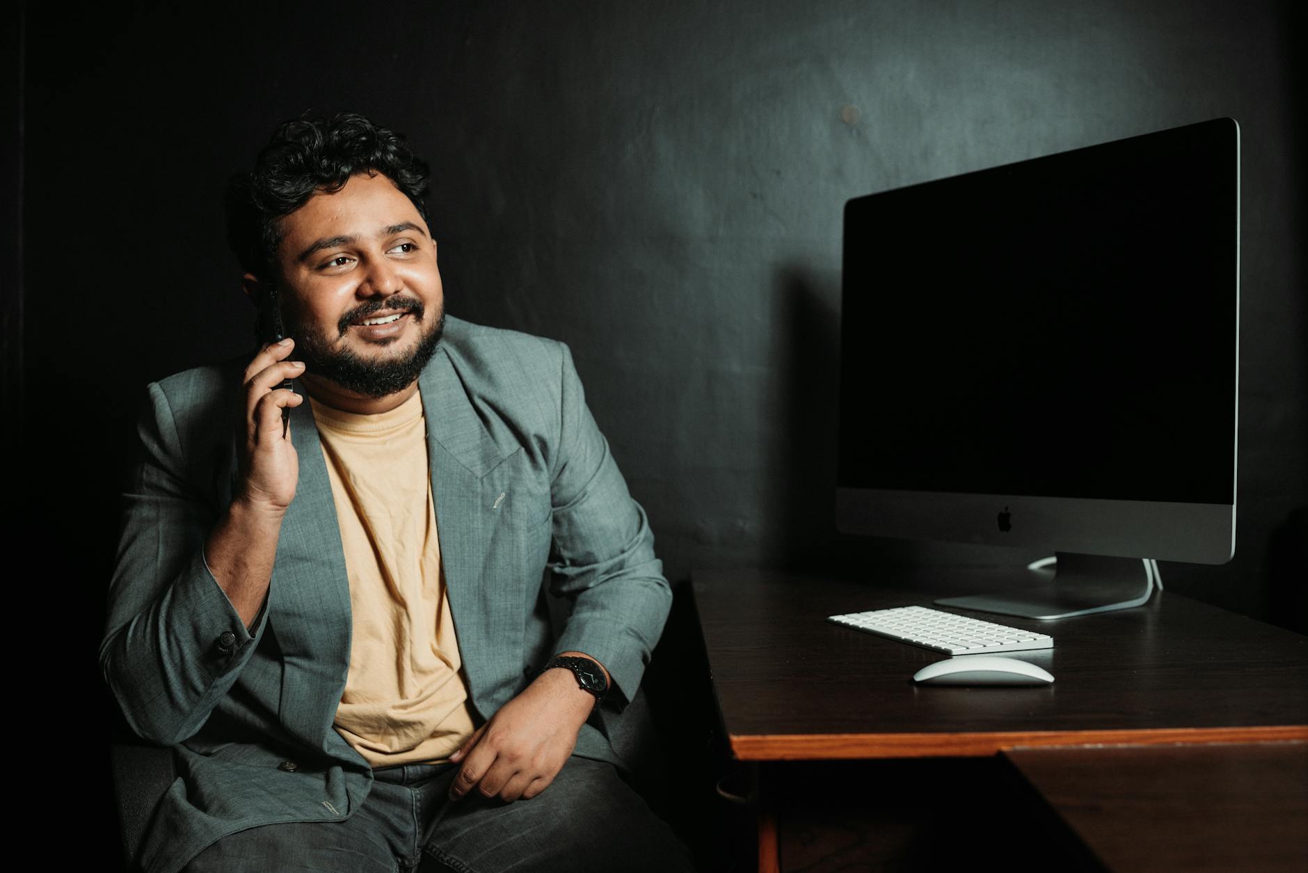Professional man in a suit using a smartphone at a desk with a computer in a modern office.