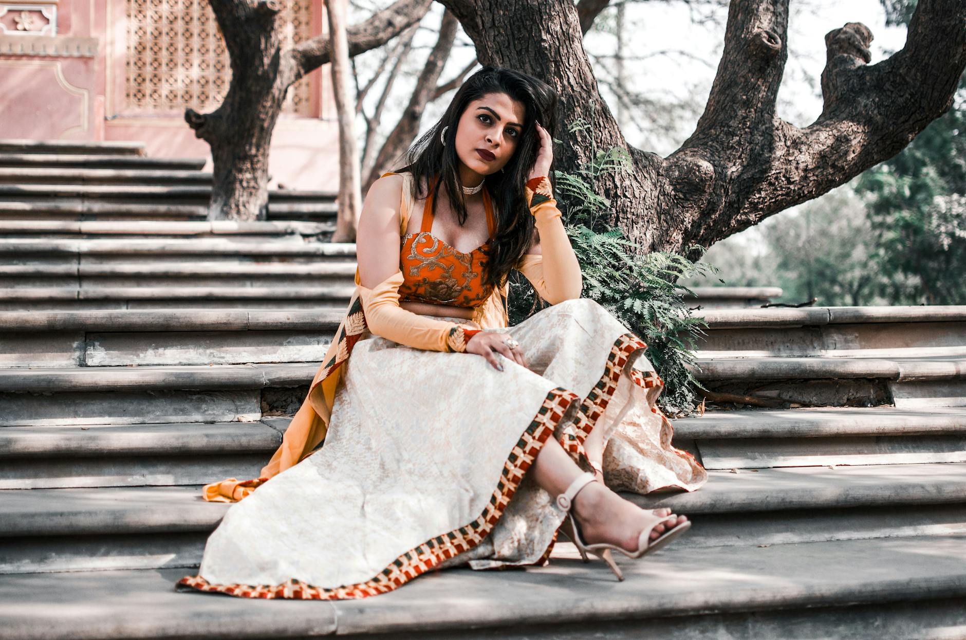 A woman elegantly seated on stone steps amidst nature, wearing traditional attire.