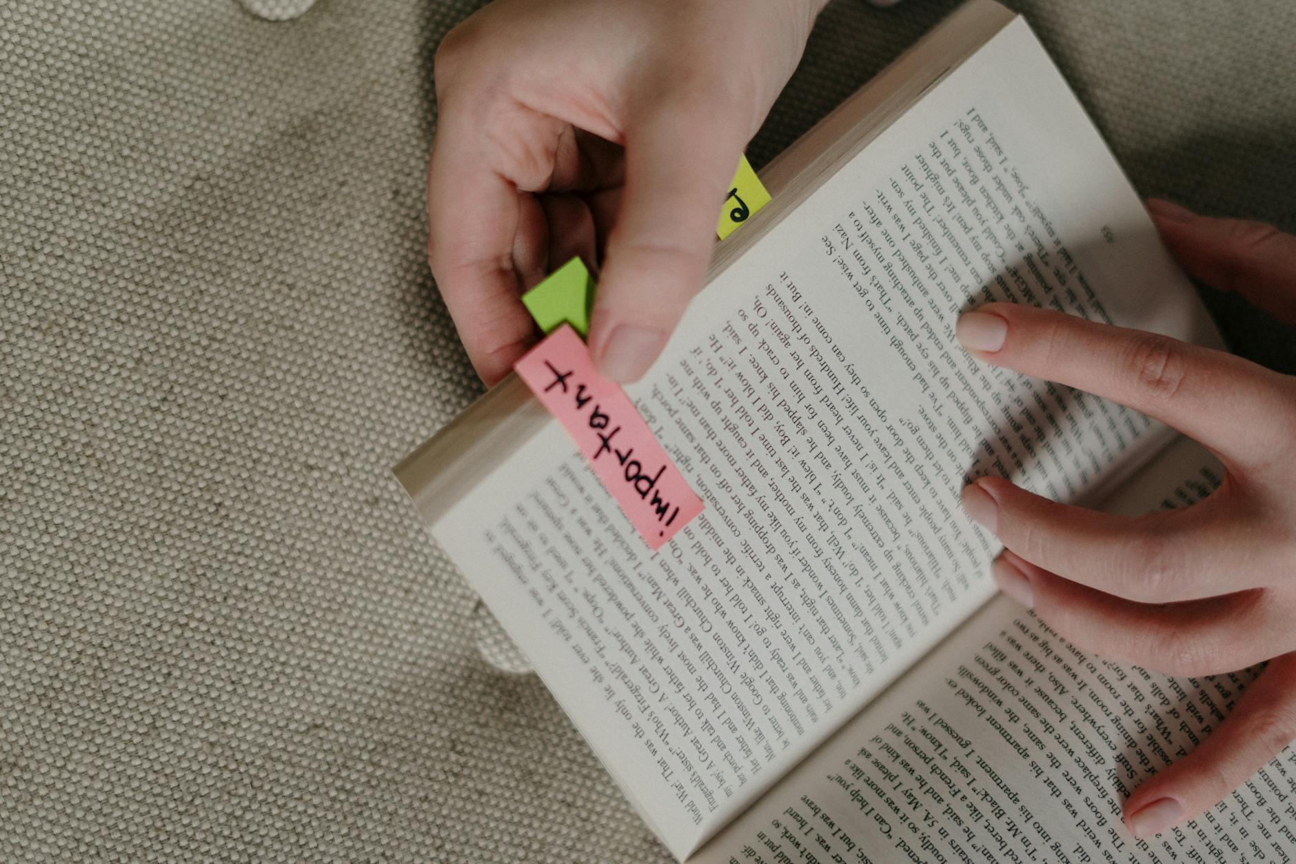 A close-up image of hands marking a book with colorful sticky notes for emphasis.