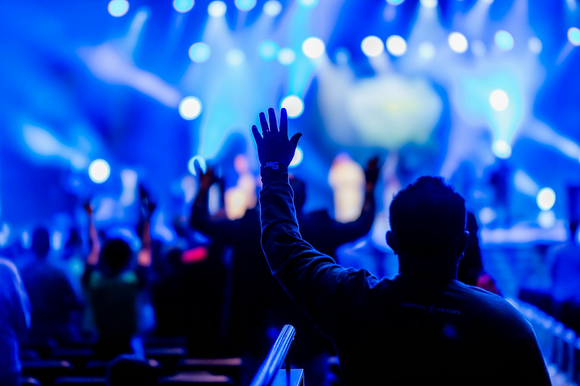 Vibrant concert scene with audience raised hands and dramatic blue lighting.